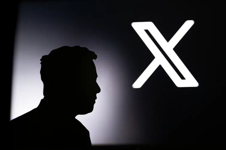 Elon Musk's silhouette in front of a projection of the X logo.