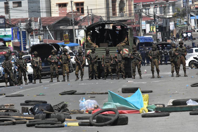 Soldiers of the Myanmar army standing in a line on a road.