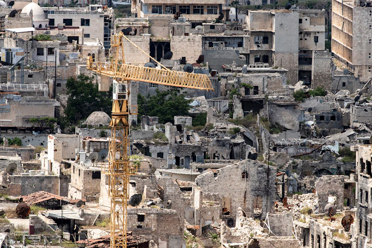 Une grue au premier plan avec des immeubles en ruine