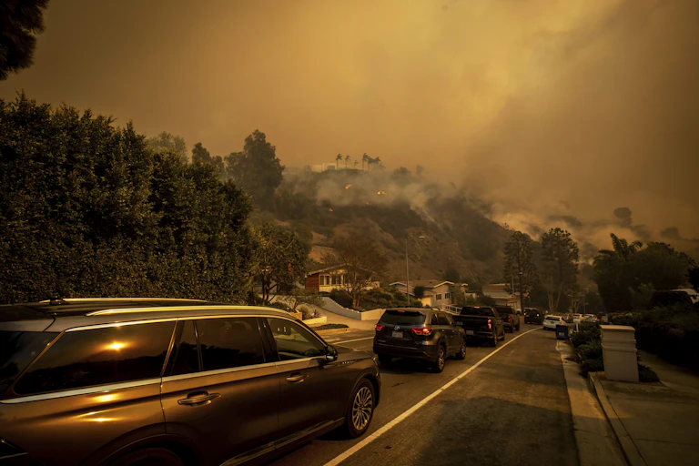 Cars drive past homes next to a burning hillside in the Los Angeles area.