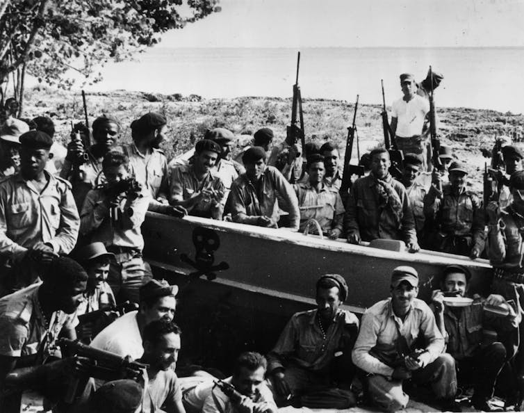 black and white photo of armed men around a boat on a beach