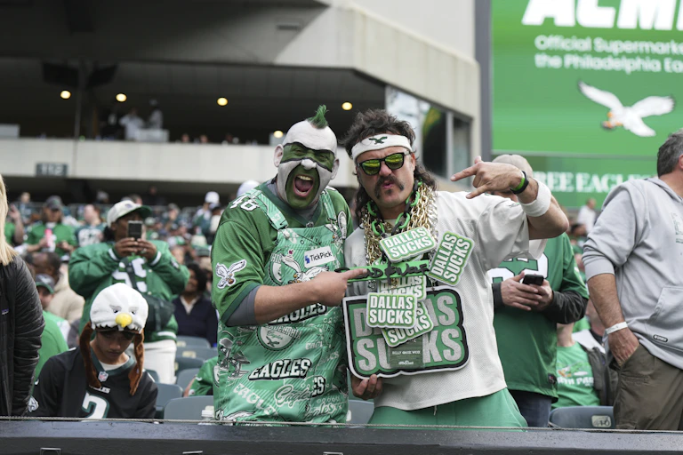 Man in green and white face paint and wearing Eagles jersey and Eagles overalls poses with man wearing Eagles sweatband and at least a half dozen chains around his neck that read "Dallas sucks"