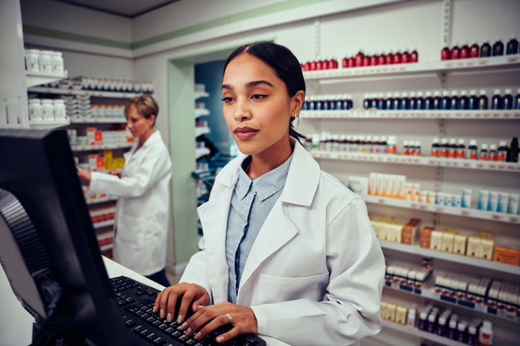 Pharmacist typing at computer behind the counter