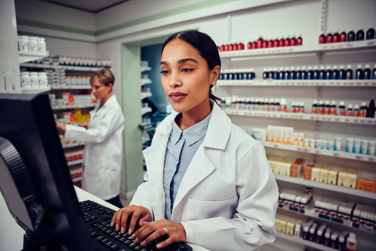 Pharmacist typing at computer behind the counter