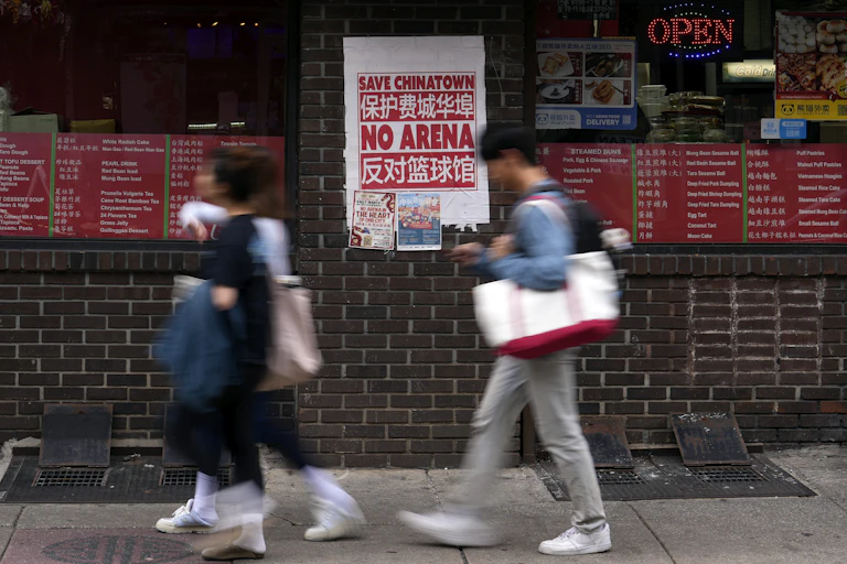 Pedestrians walk past a sign on street that reads: 'Save Chinatown - No Arena'