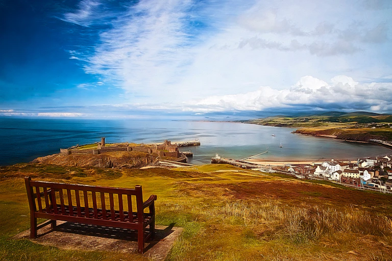 wooden bench on coast, overlooking bay with town and blue sea