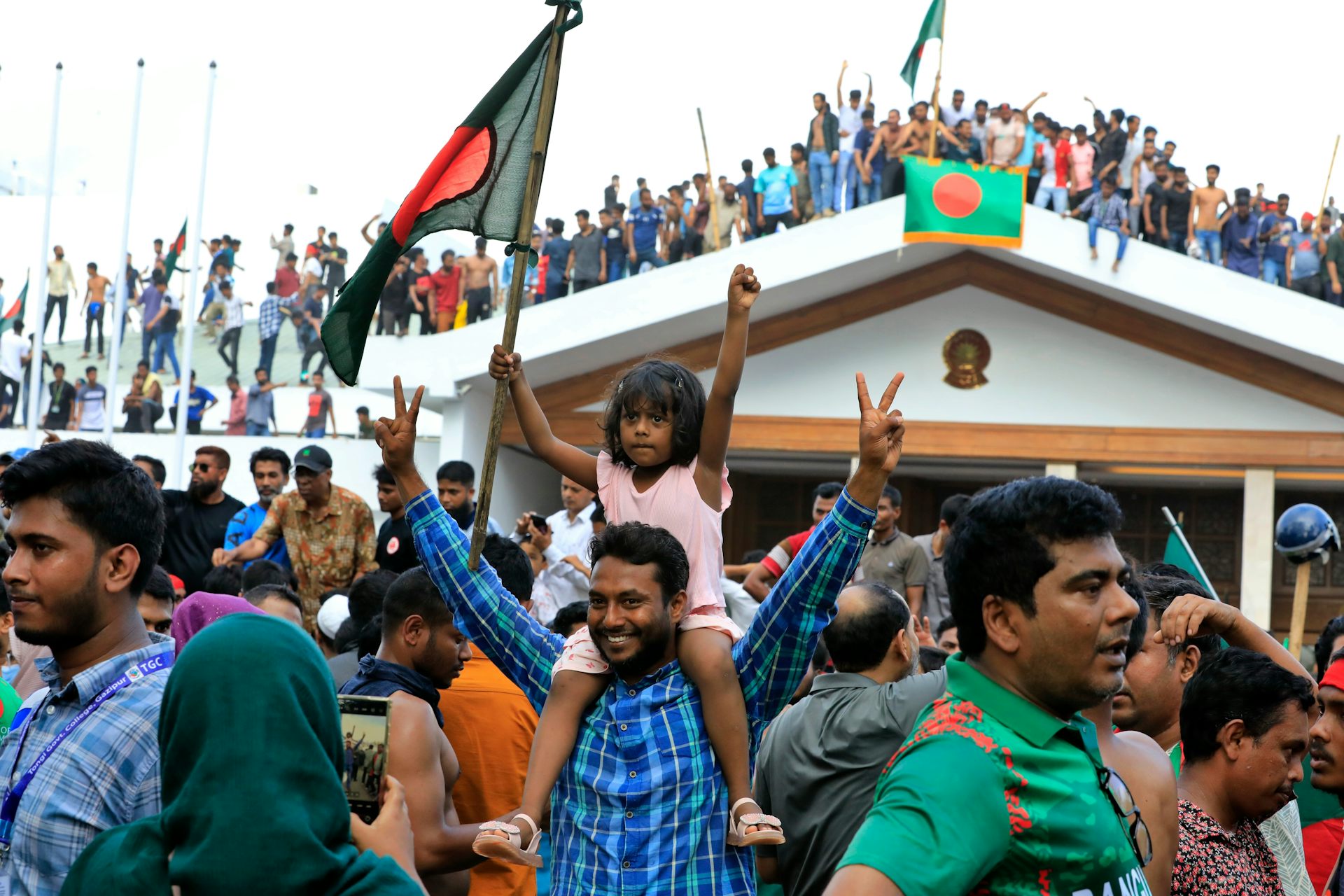 Des manifestants brandissent des drapeaux bangladais, un homme tient sur ses épaules une petite fille en faisant le signe de la victoire