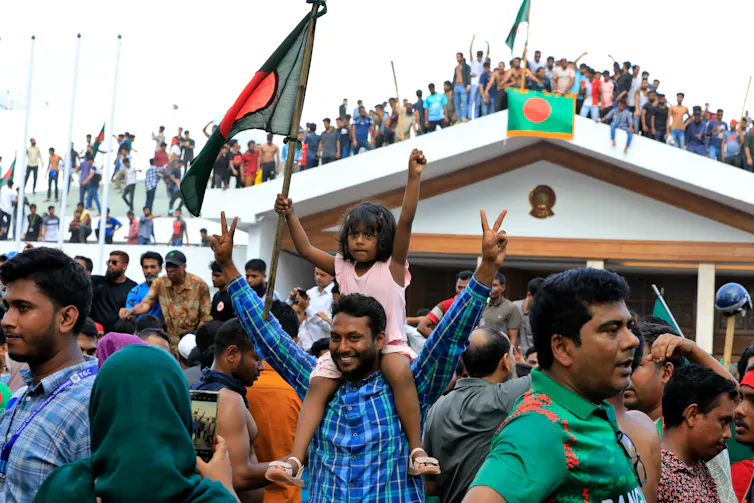 Des manifestants brandissent des drapeaux bangladais, un homme tient sur ses épaules une petite fille en faisant le signe de la victoire