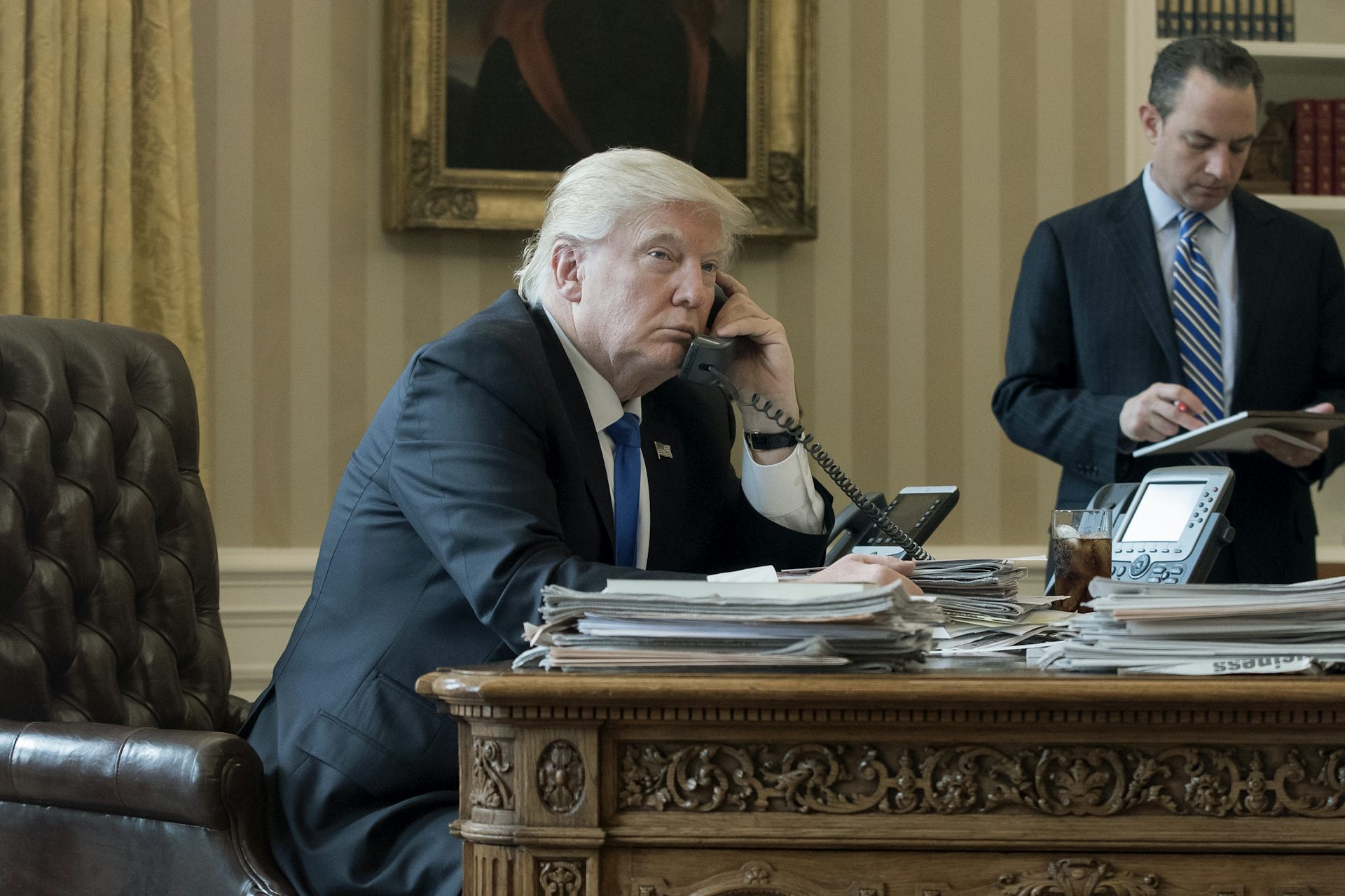 Donald Trump on the telephone in the Oval Office with an aide in the background, January 2017.