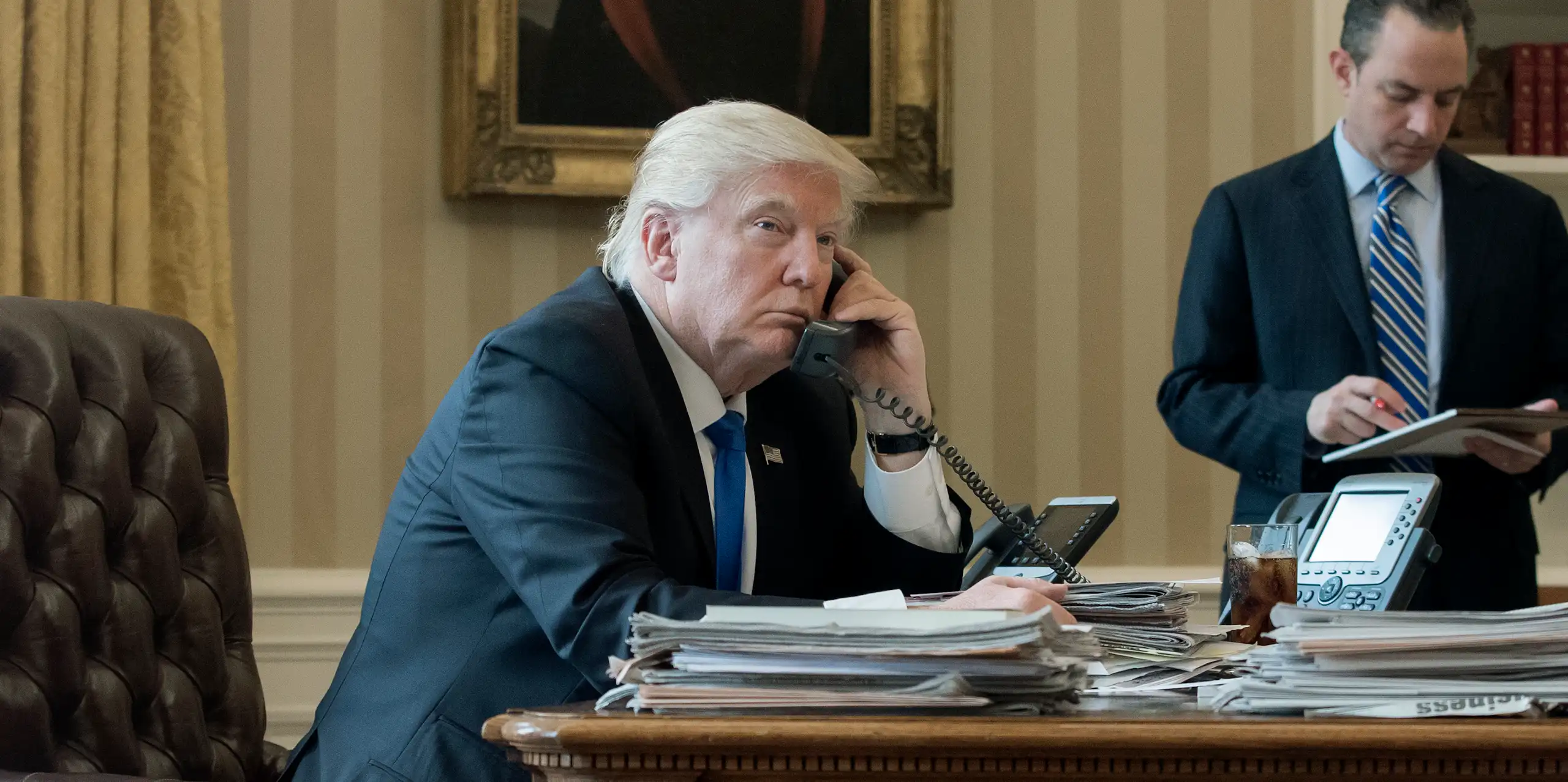 Donald Trump on the telephone in the Oval Office with an aide in the background, January 2017.