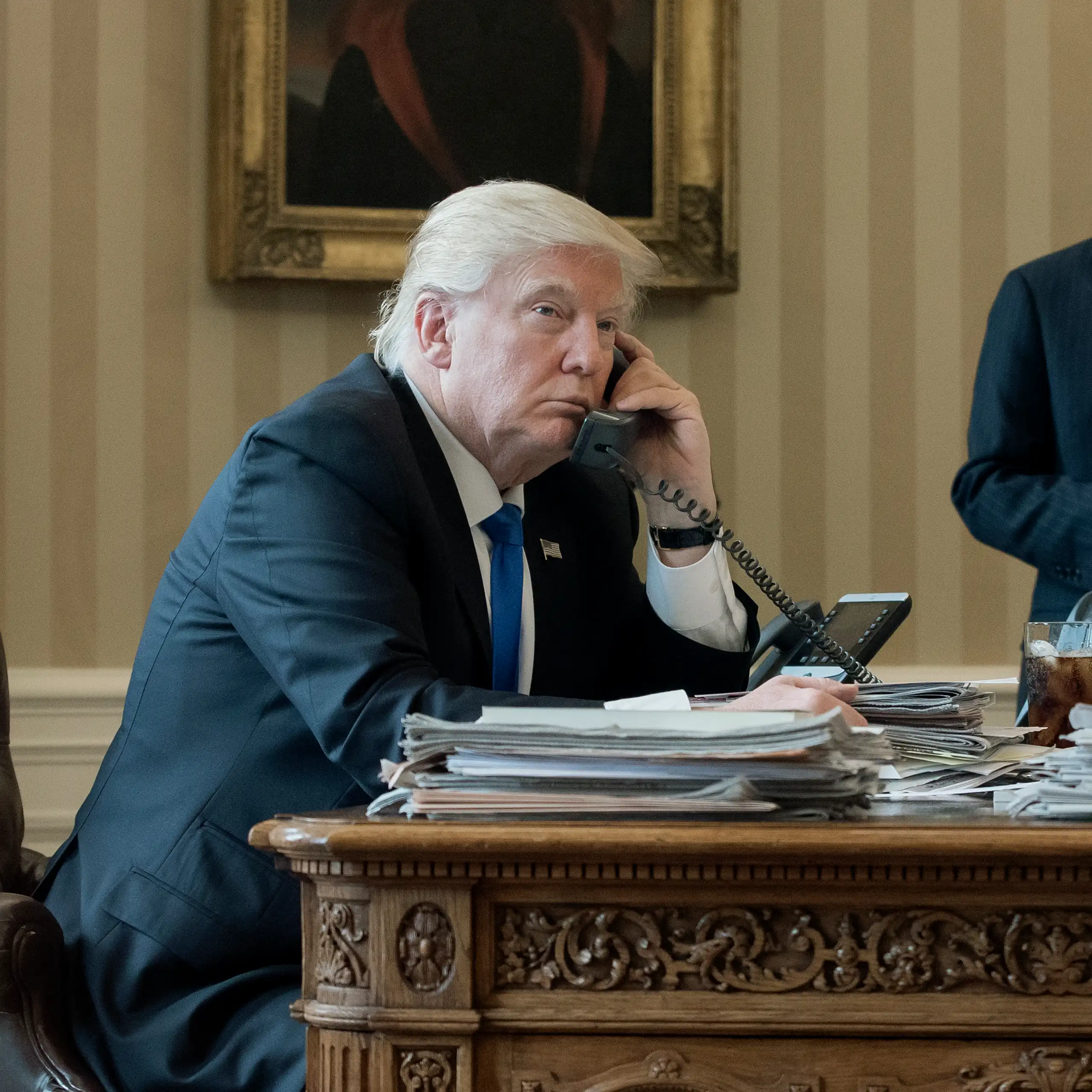 Donald Trump on the telephone in the Oval Office with an aide in the background, January 2017.