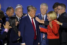 Donald trump surrounded by people raising their hands in prayer