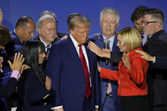 Donald trump surrounded by people raising their hands in prayer