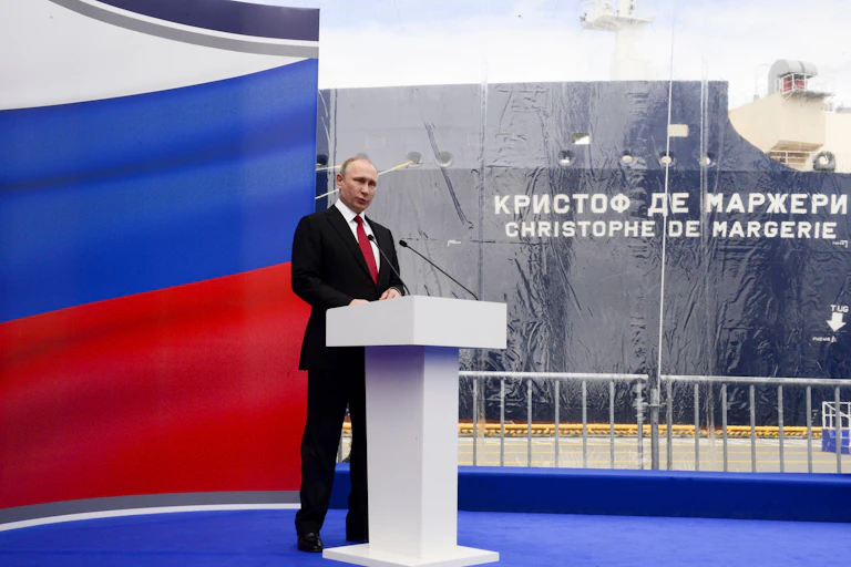 Vladimir PUtin at a podium with a Russian flag. In the background is the Christophe de Margerie LNG carrier.