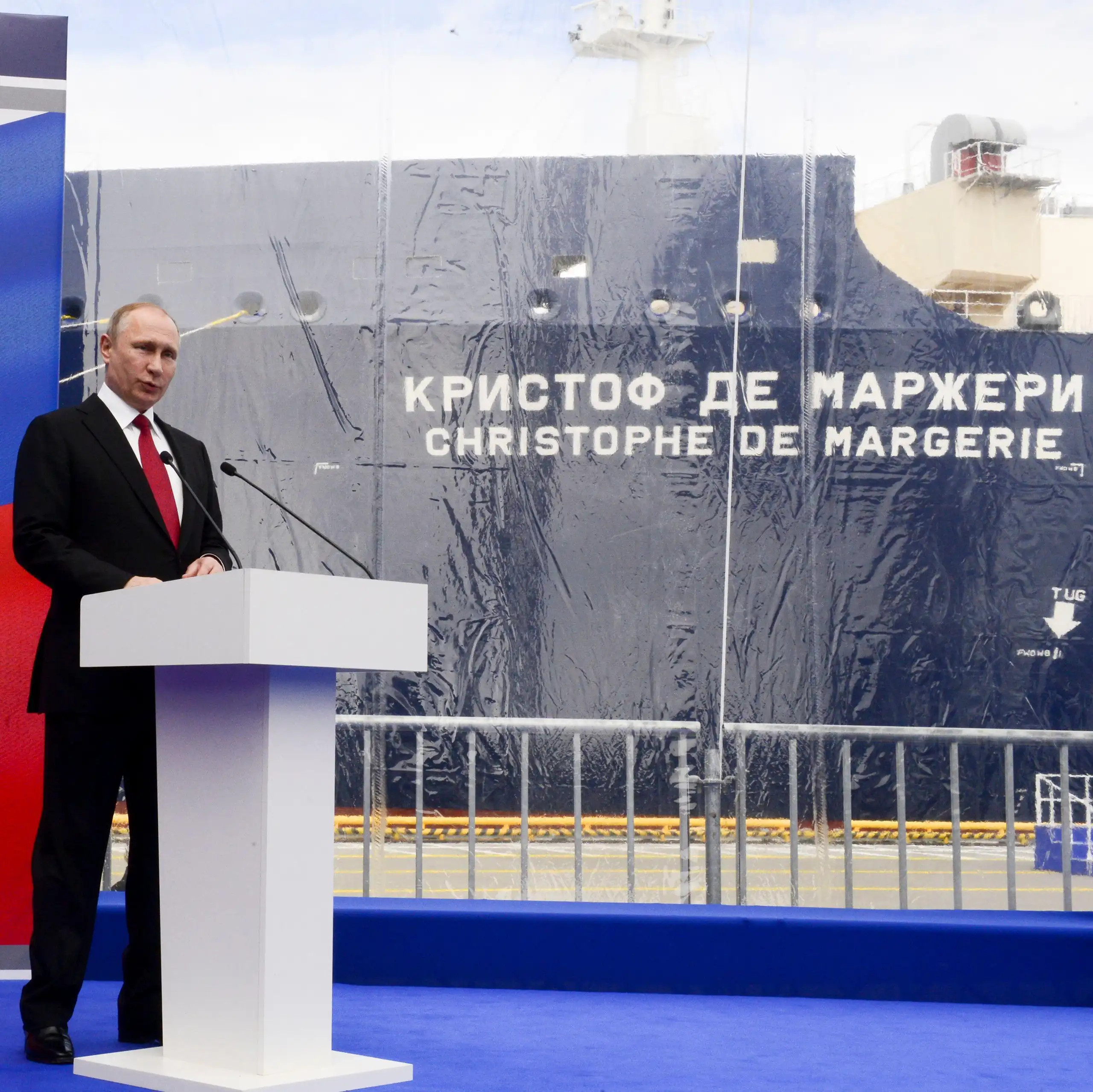 Vladimir PUtin at a podium with a Russian flag. In the background is the Christophe de Margerie LNG carrier.
