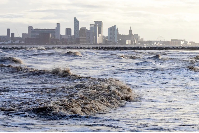 rough waves on river with liverpool city skyline in background, grey skies