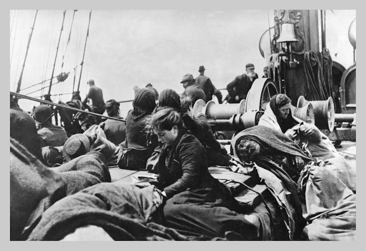 Women in a black and white photo from a long time ago, sit on the deck of a ship.