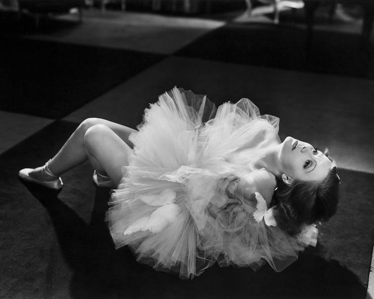 A glamorous woman reclines on the floor in a dancer's costume in an old black and white photo.