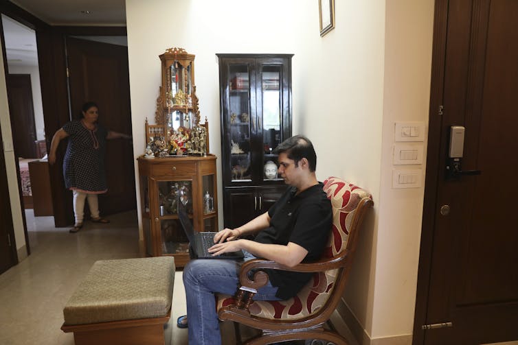 Man works on a laptop in a sparsely furnished living room.