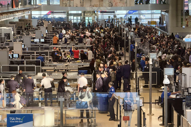 An overhead view of a crowd of people passing through lines and lanes at an airport.