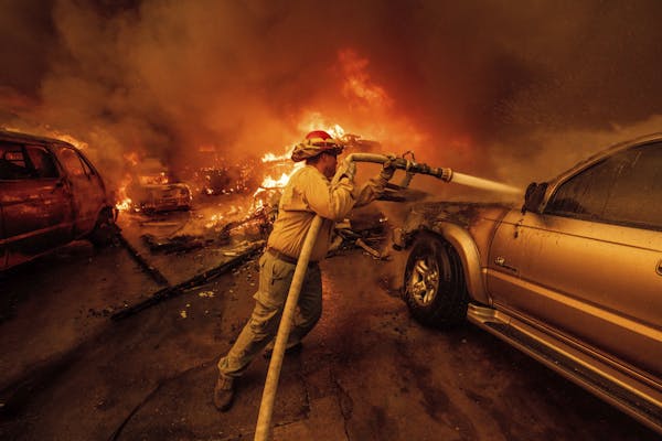 A firefighter works to keep a car from burning as flames spread nearby.