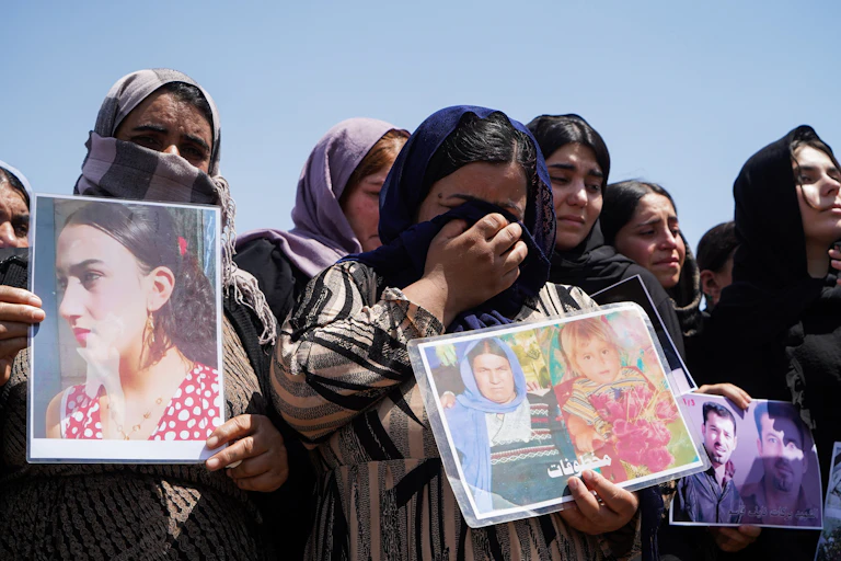 Women in headscarves, many in tears, hold photos.