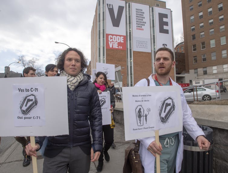 people at a protest carry signs featuring a coffin with a handgun on top of it