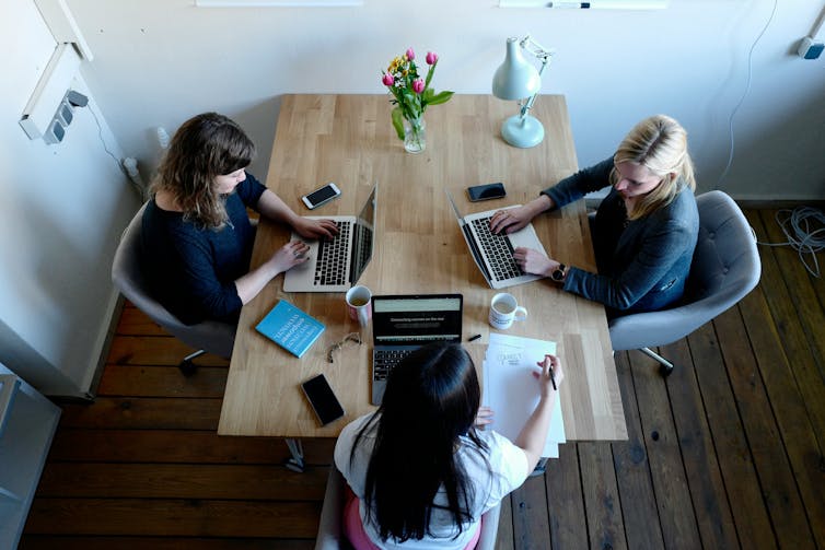 Three women working on laptops and sitting around table