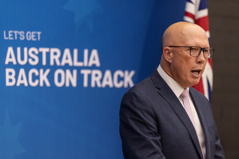 A man in glasses and a suit speaks in front of a blue backdrop saying let's get Australia back on track