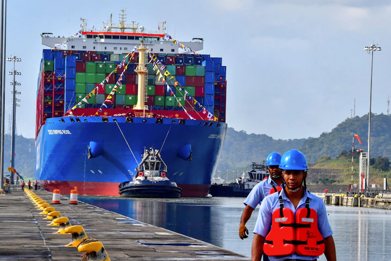 A large cargo ship is seeing being tugged down a canal.