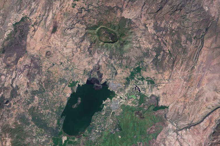 A satellite image that shows a big depression amid a brown and green landscape. There is also a large body of water visible