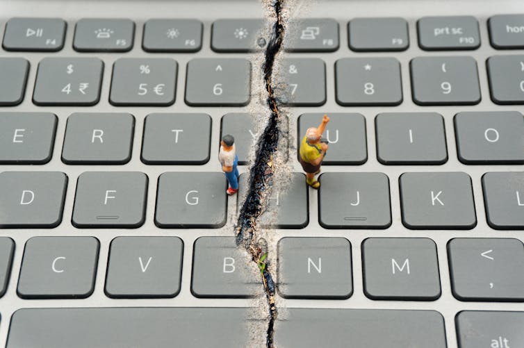 A keyboard with a dividing crack down the middle, and two miniature figurines standing on either side