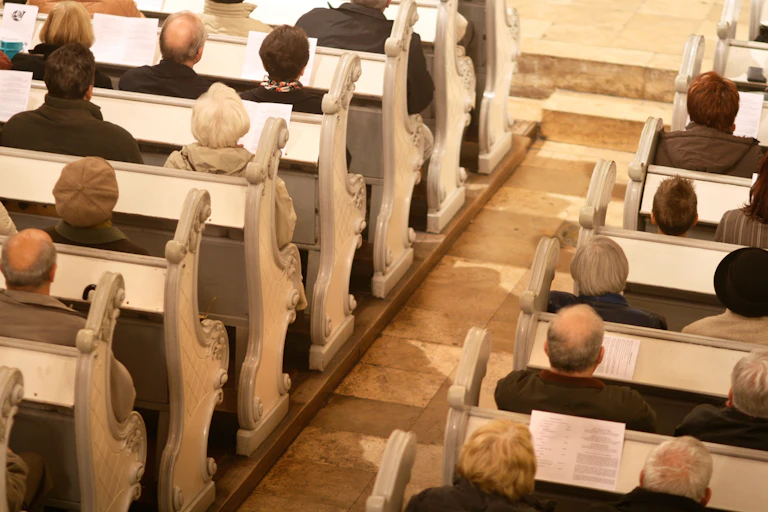 Several rows of white church pews, with about a dozen people sitting on them.