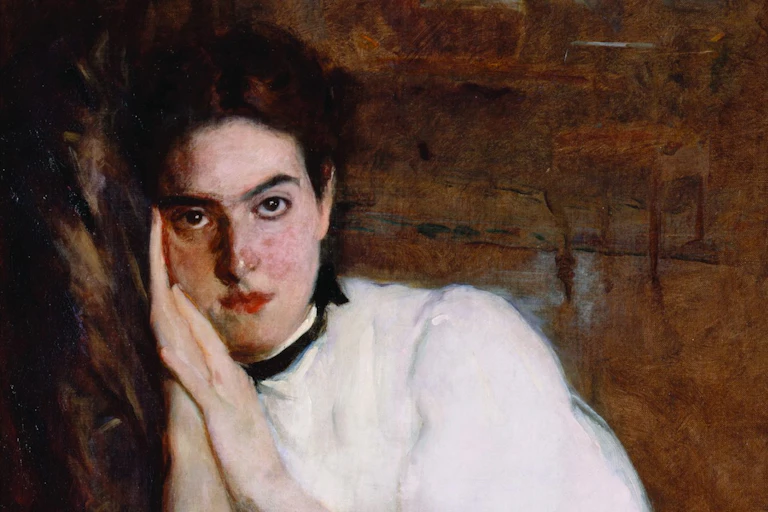 Portrait of a woman with her hands beside her face, looking directly at the viewer, she seems lost in thought.