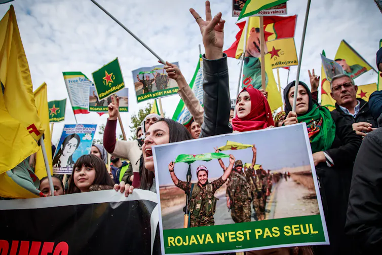 Kurdish women waving flags and a banner depicting a female Kurdish soldier.