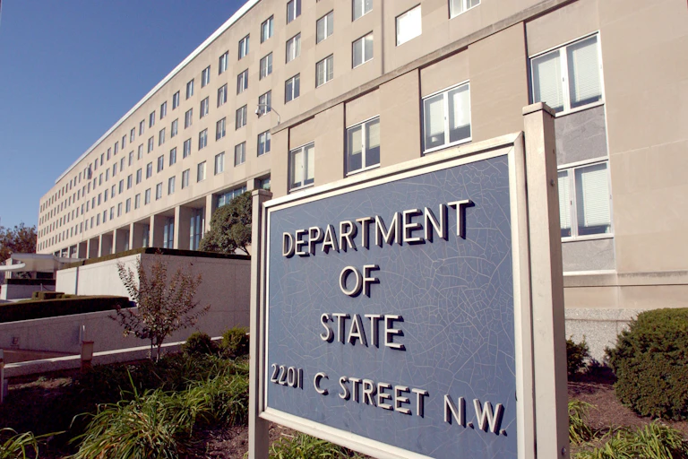 A sign that says 'Department of State' is in front of a large beige building with windows.