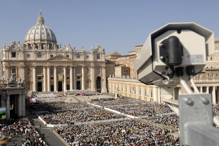 Surveillance camera overlooking a large crowd of people in front of a historical building.
