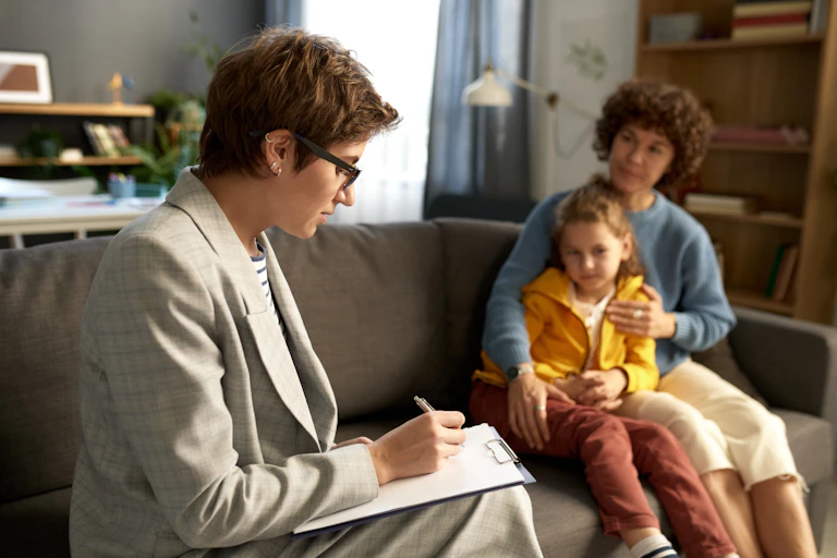 Social worker making notes in document while talking to difficult child and his mom at home.