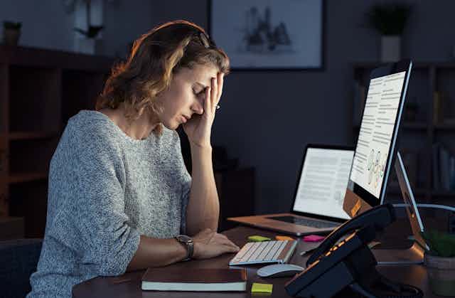 Une femme assise devant un ordinateur à un bureau repose sa tête sur sa main.