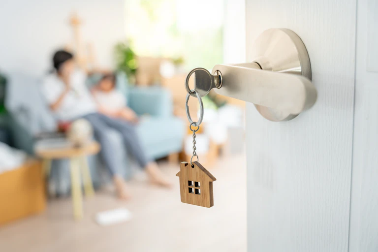 A key in door, blurred people sit on couch in background