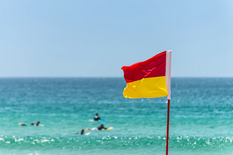 Red and yellow Warning Sign Flag marking the limit of the safe swimming area on a beach under a blue summer sky in Australia.