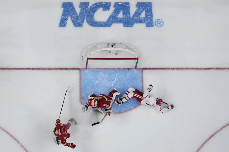 Overhead view of a hockey player in a white jersey scoring a goal against a goalie in a red jersey
