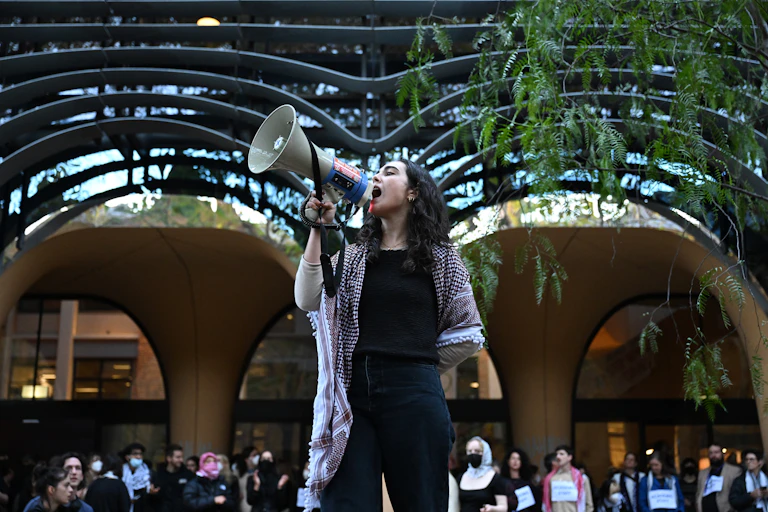 A woman stands at a university and speaks into a megaphone
