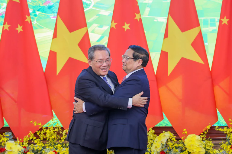 Deux hommes se font une accolade devant des drapeaux vietnamiens et chinois.
