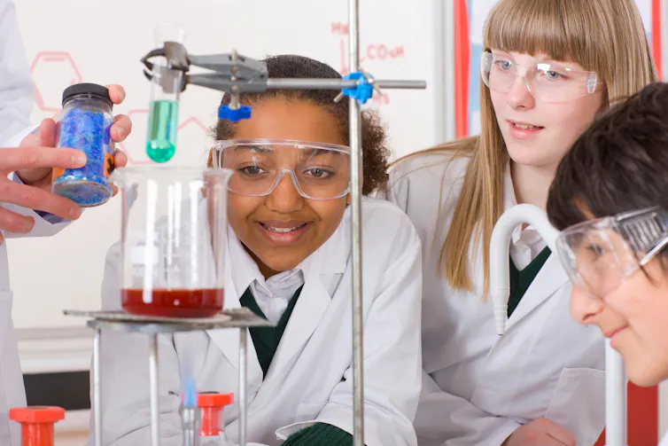 Pupils in science lesson wearing lab coats and safety glasses