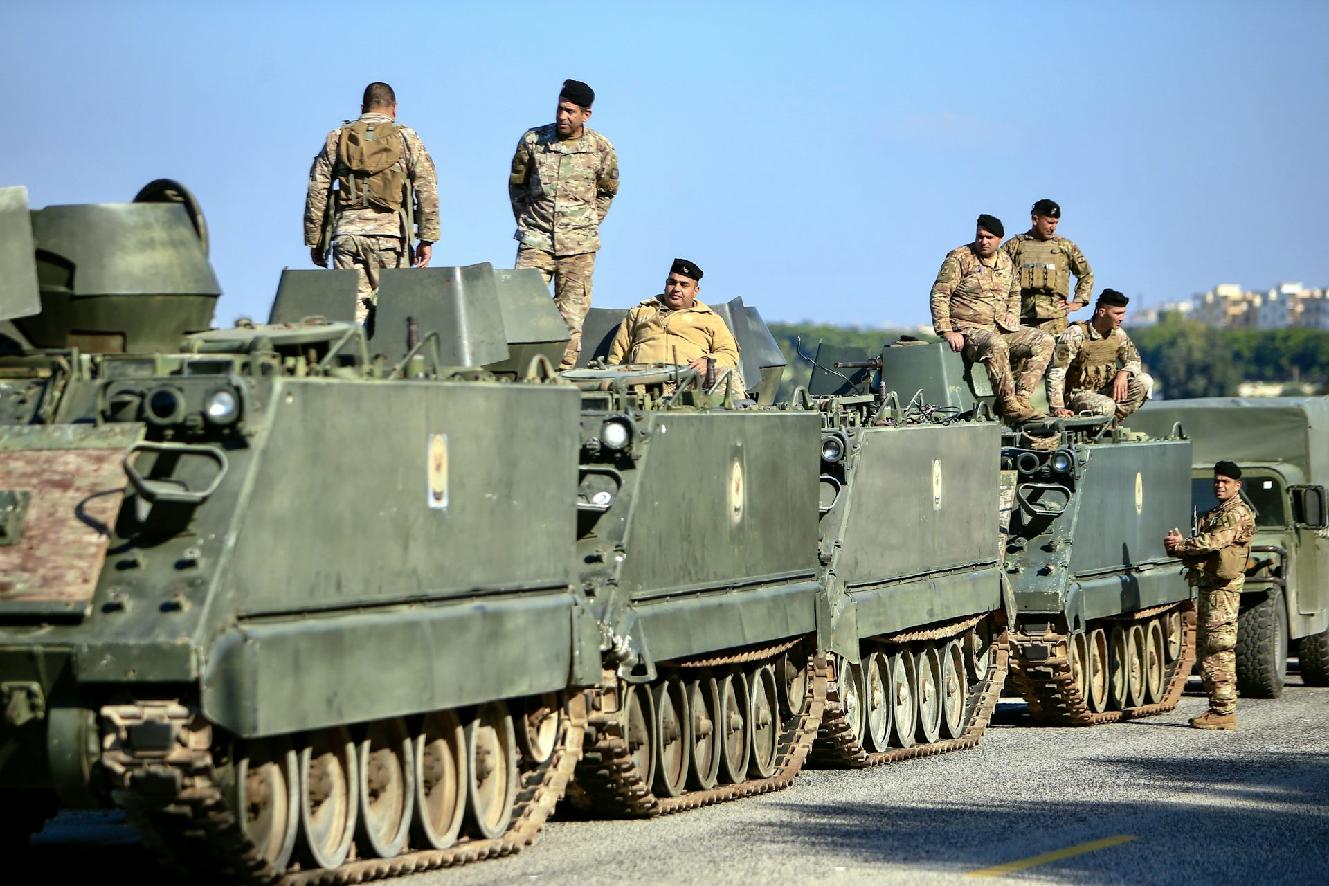 Lebanese soldiers riding atop armoured vehicles.