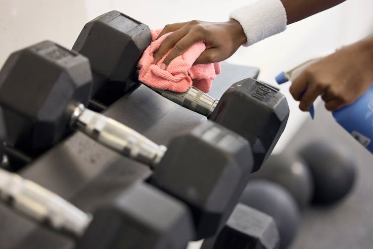 A person cleans off dumbbells with disinfectant and a microfibre cloth.