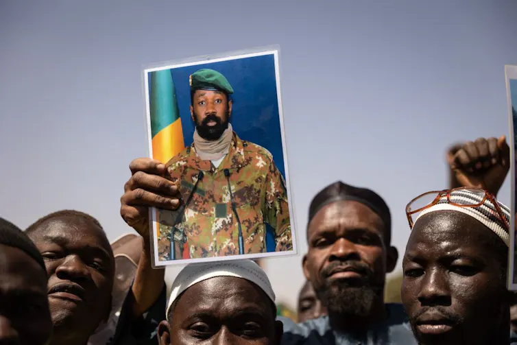 A group of African men, one of them holding up a photo of a bearded man in a military uniform.