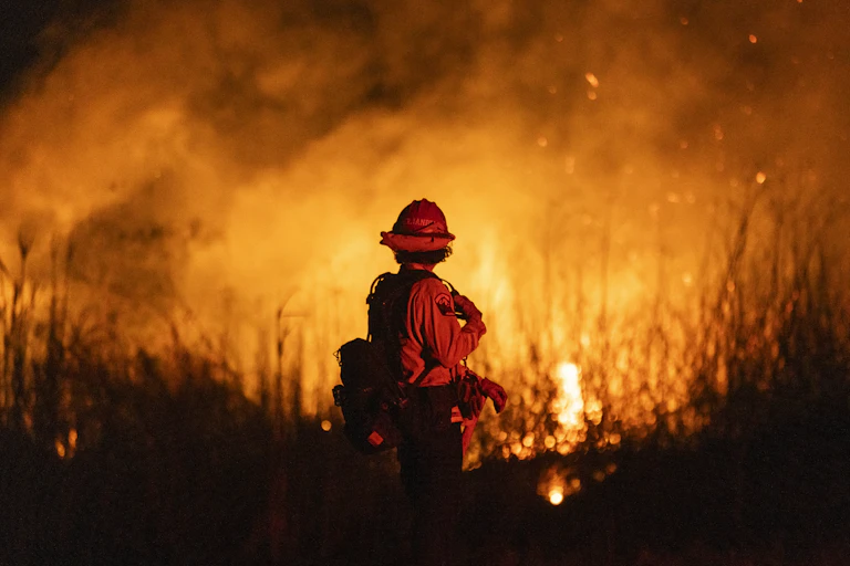 pompier de dos face à un paysage en flammes de nuit