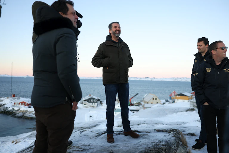 Several men dressed for winter stand on a snowy patch near the ocean.